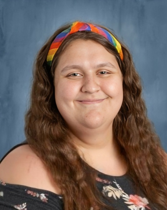 A headshot of a woman with a rainbow headband, long brown hair, and on a blue background